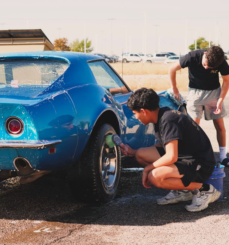 Two technicians hand washing a blue classic Corvette