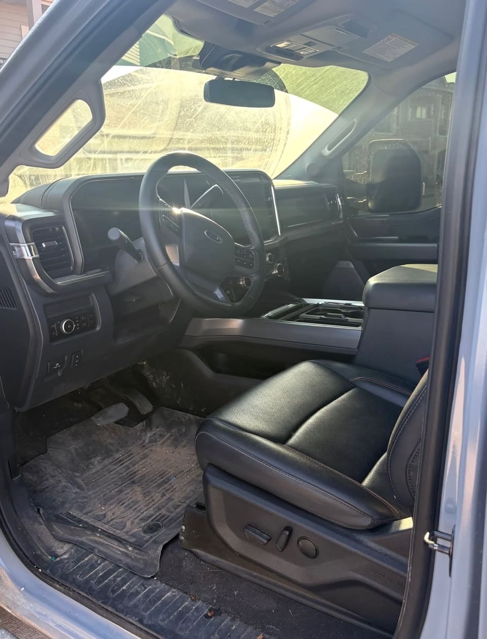 A truck cab interior before detailing: dust and grit across the floor mats and door sill, and a windscreen hazy with road film.