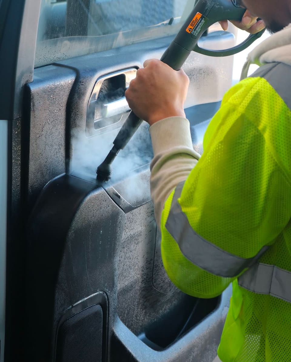 A technician steam cleaning the door card of a work truck