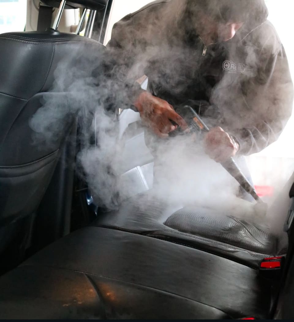 A technician steam cleaning a car seat